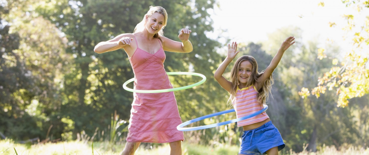 Woman and young girl outdoors using hula hoops and smiling